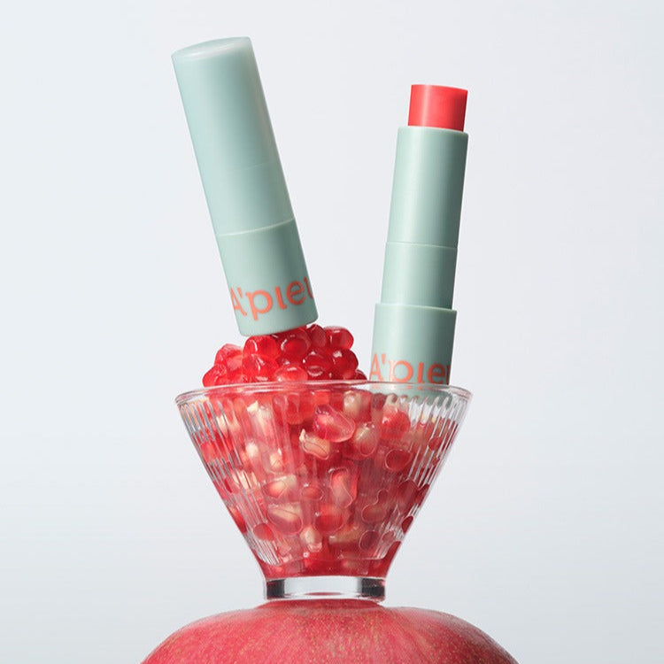 A'PIEU Juicy Pang Care Lip Balm : baume à lèvres vert sur décor de fruits rouges, marque A'PIEU, fond clair.