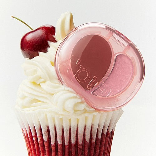 A'PIEU Juicy Pang Mood Blending Lip & Cheek Balm, packaging rose sur muffin, cerise et fleurs blanches en fond clair