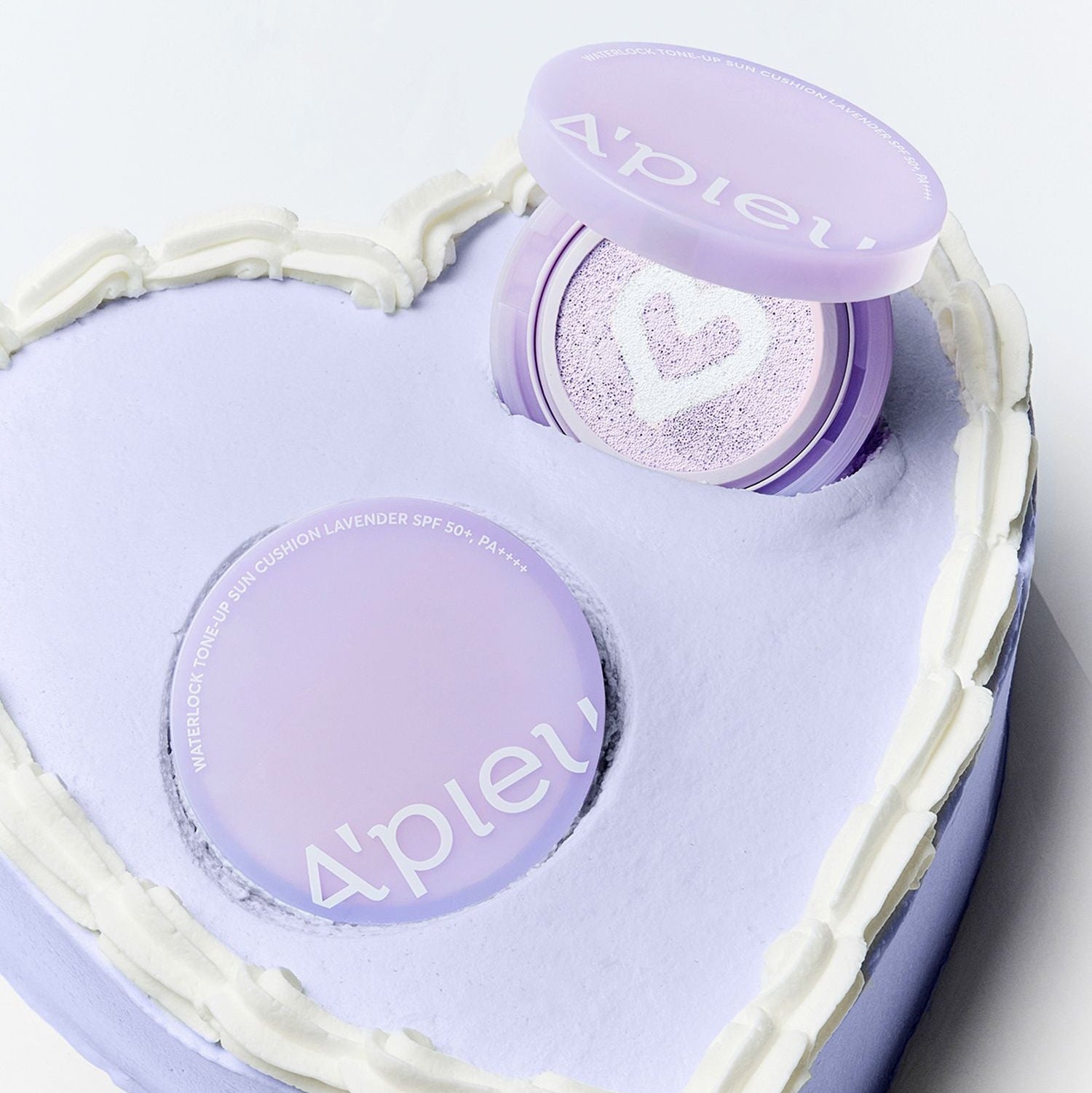 Décris l’image en français : A'PIEU Waterlock Tone-Up Sun Cushion Lavender 15g, coussin hydratant lavande, boîte ouverte sur fond clair.