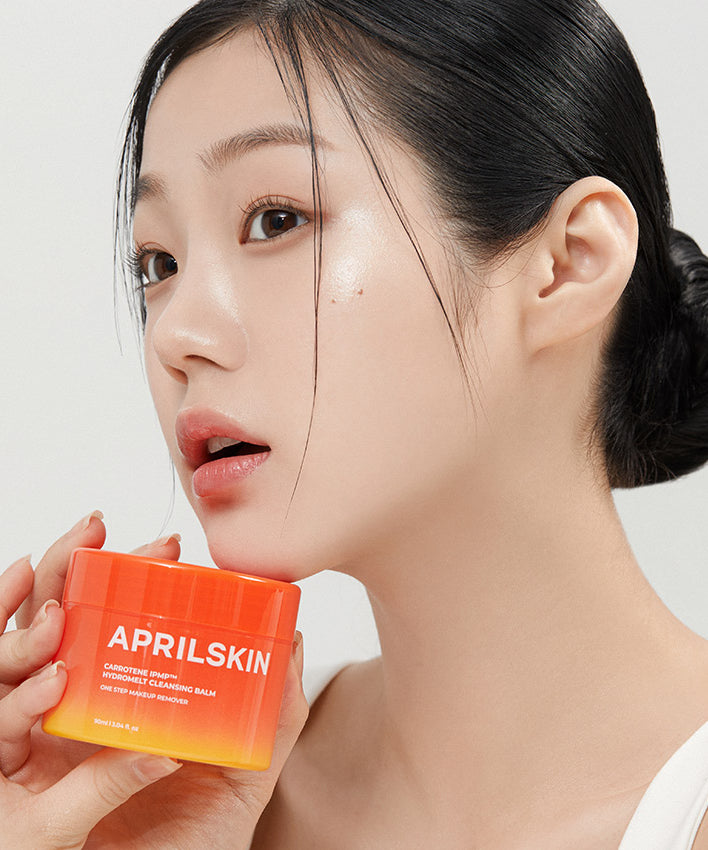 Femme tenant le APRILSKIN Carotene Melting Cleansing Balm, nettoyant visage en pot orange.