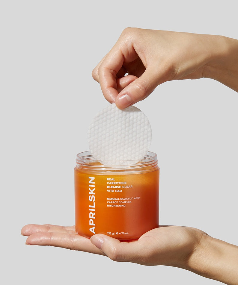 Main d'une personne tenant un disque APRILSKIN Carrotene Clarifying Vita Pad sorti d'un pot. Soin clarifiant à la carotène pour une peau éclatante.
