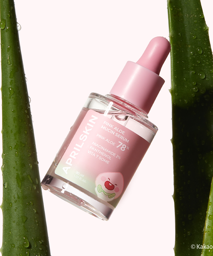 APRILSKIN Pink Aloe Mucin Serum entre deux feuilles d'aloès, flacon rose avec compte-gouttes. Hydratation et soin de la peau.