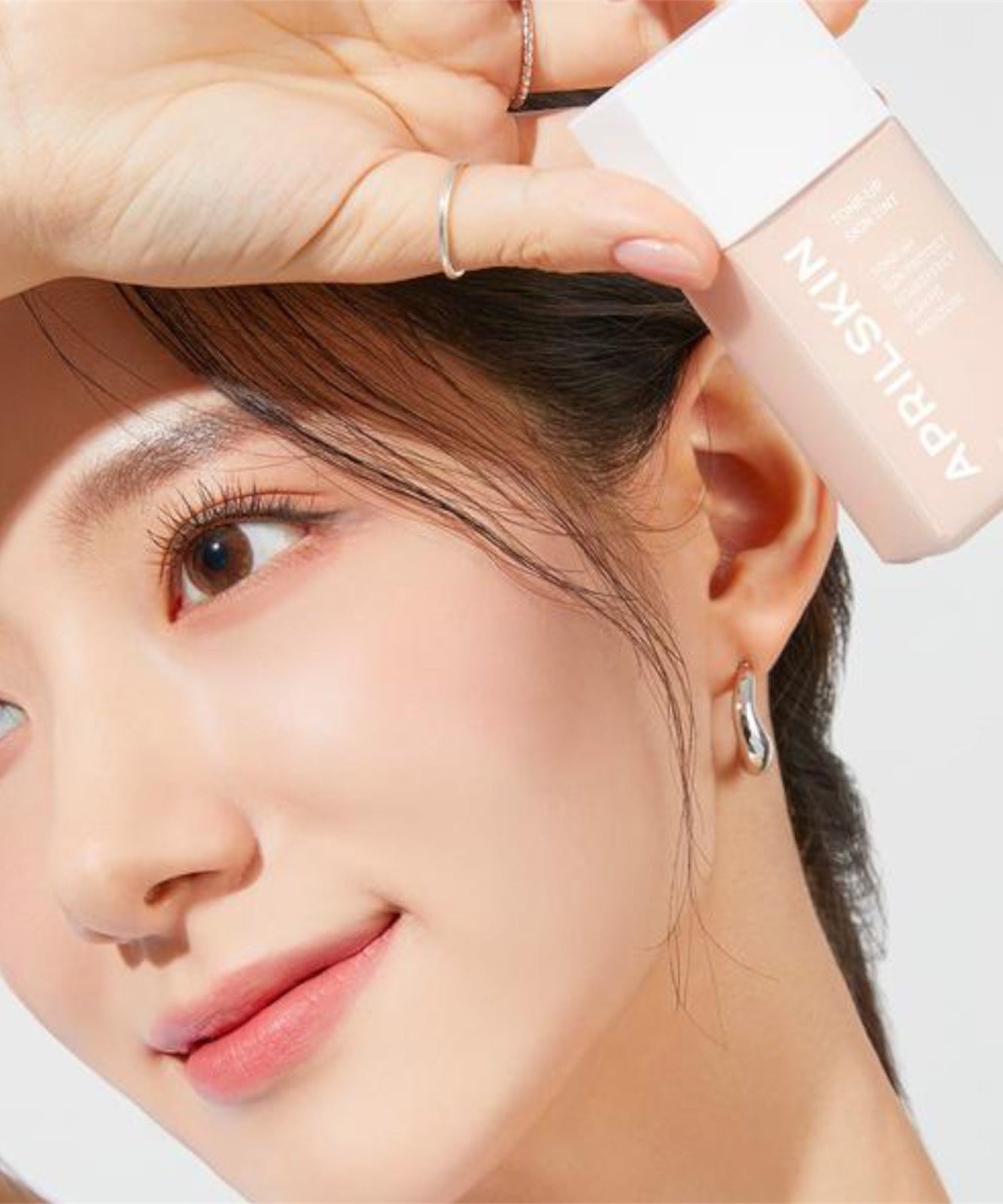 Femme tenant APRILSKIN Tone-Up Skin Tint pour un teint éclatant et naturel avec un fini doux et lumineux.