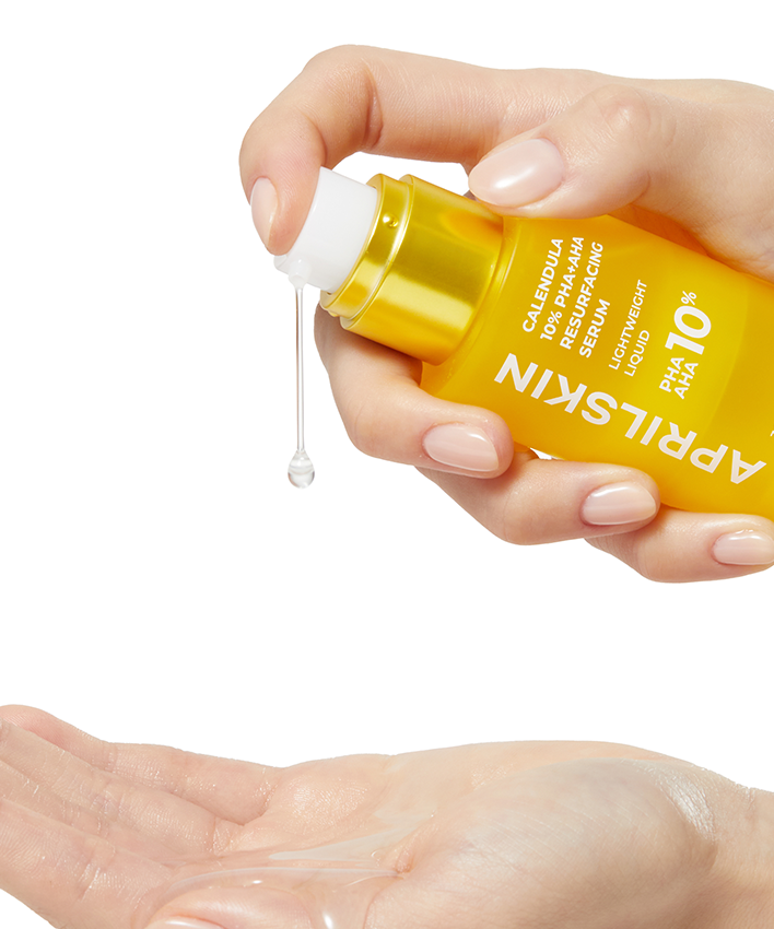 APRILSKIN Calendula 10% PHA+AHA Resurfacing Serum 30ml : main tenant le flacon et appliquant le sérum, fond blanc.