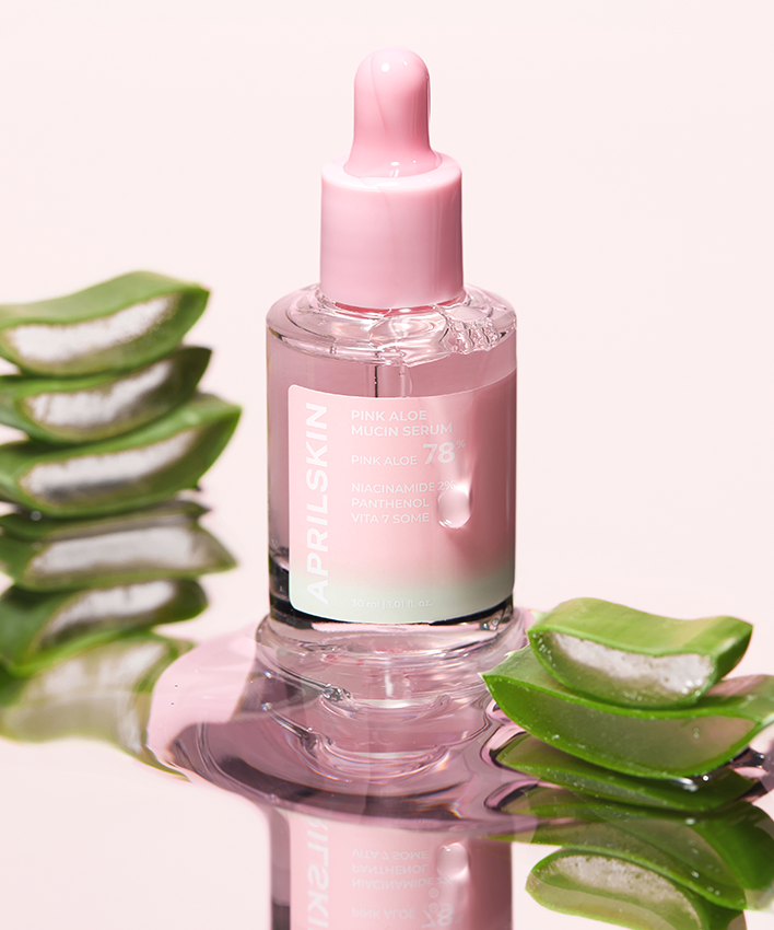 APRILSKIN Pink Aloe Mucin Serum de la marque APRIL SKIN sur fond rose, flacon et feuilles d’aloe en gros plan.