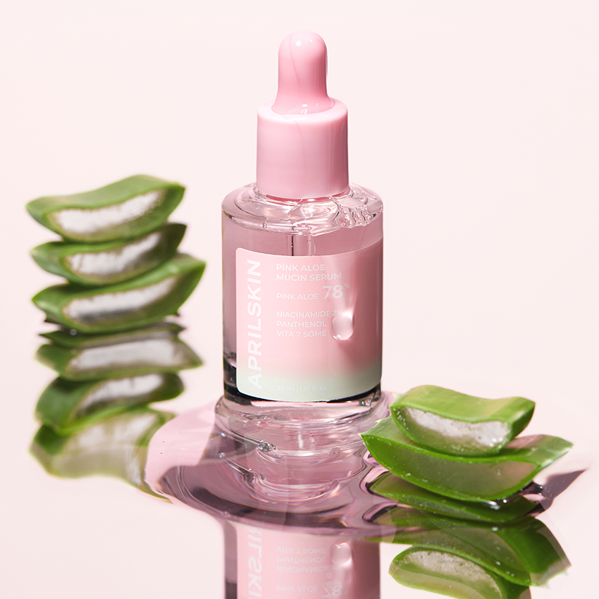 APRILSKIN Pink Aloe Mucin Serum de la marque APRIL SKIN sur fond rose, flacon et feuilles d’aloe en gros plan.