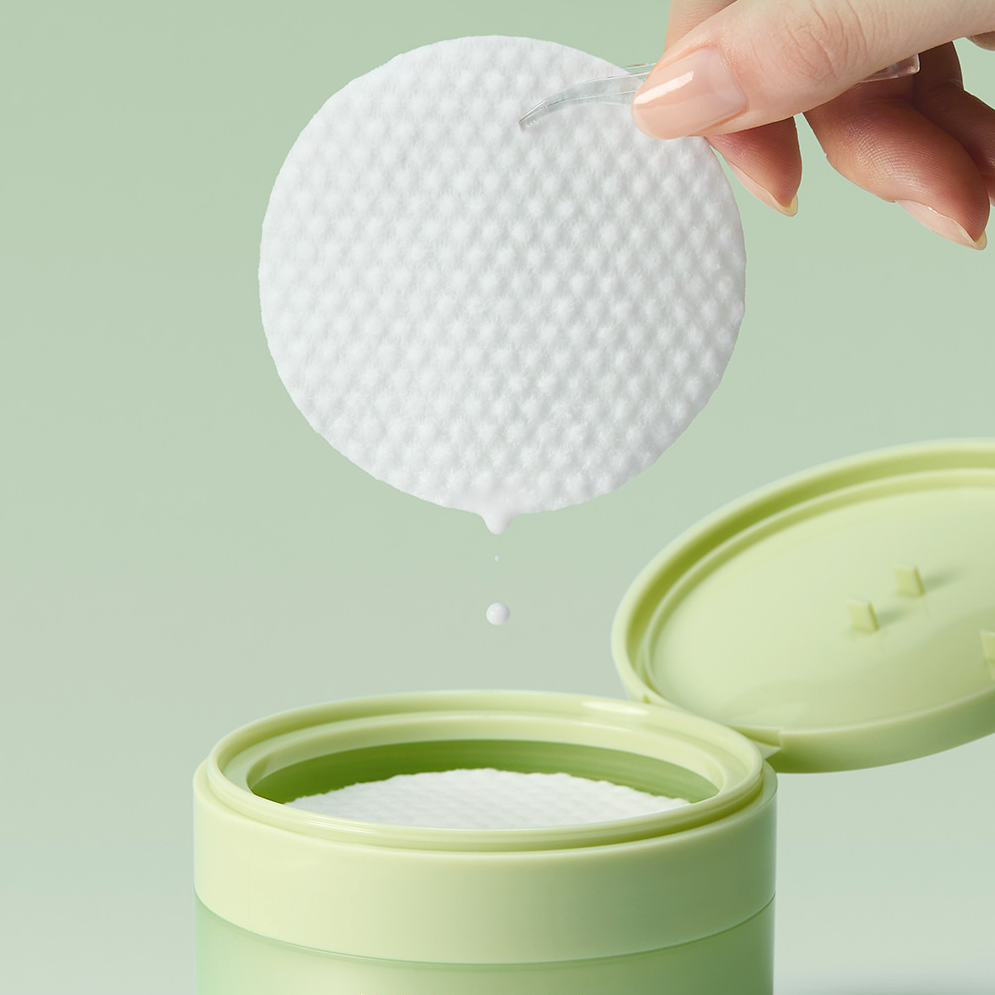 ARENCIA Pore Melt Cleansing Oil Pads 50 Sheets : main retire un pad, flacon de nettoyage, arrière-plan vert pastel.