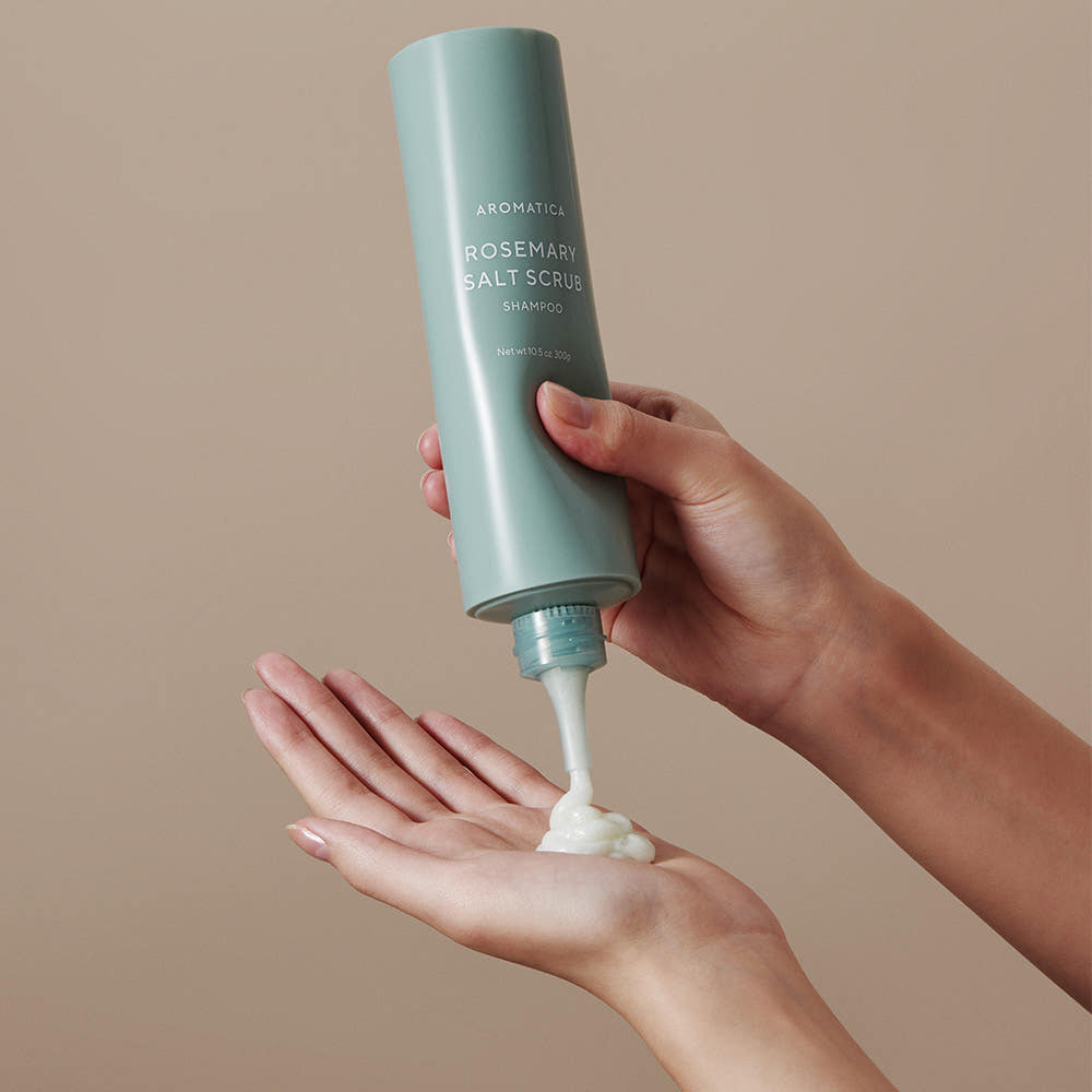 AROMATICA Rosemary Salt Scrub Shampoo, bouteille en main, crème moussante sur les paumes, fond beige minimaliste.