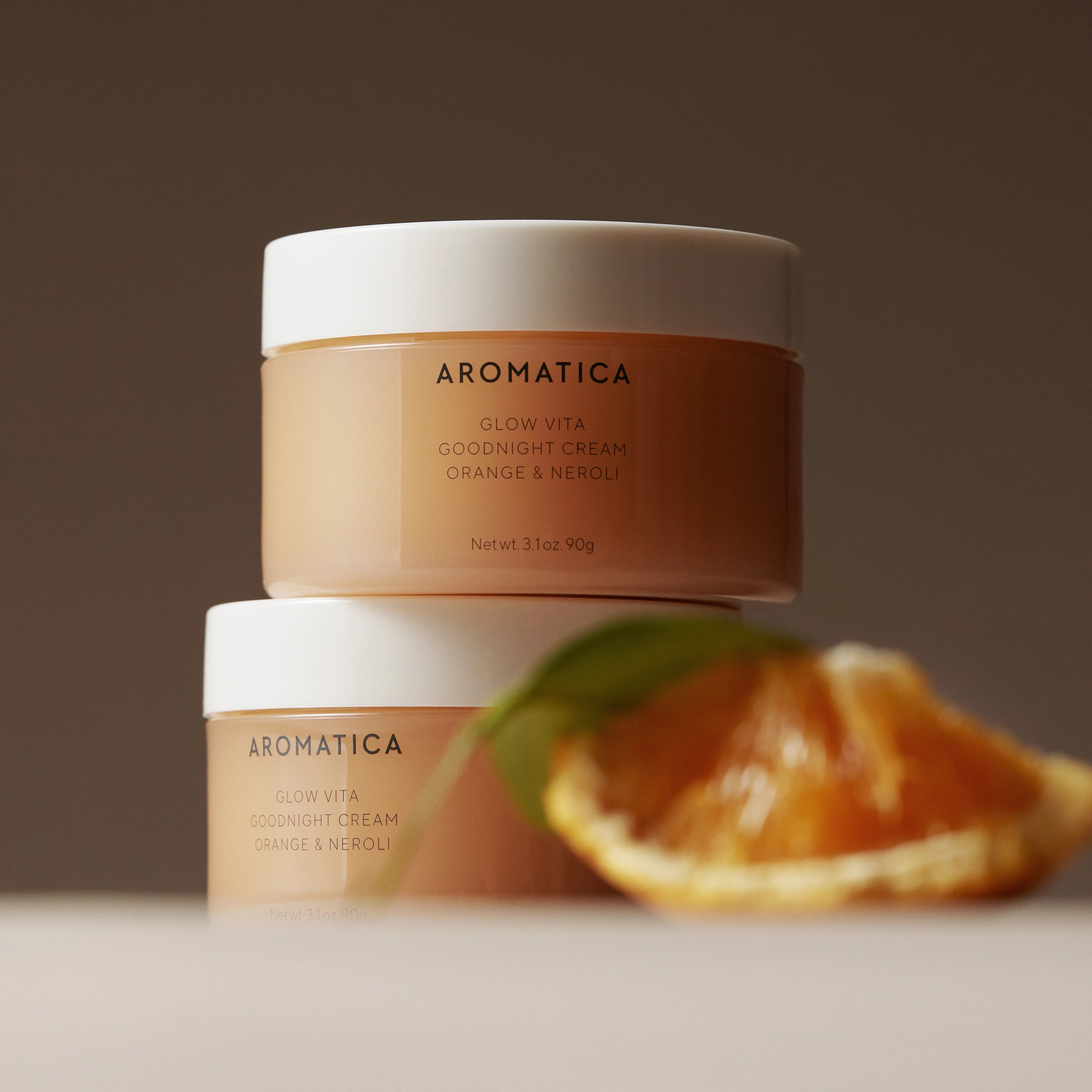 AROMATICA Glow Vita Good Night Cream Orange & Neroli 90G, crème de nuit sur fond brun avec agrume orange en arrière-plan.