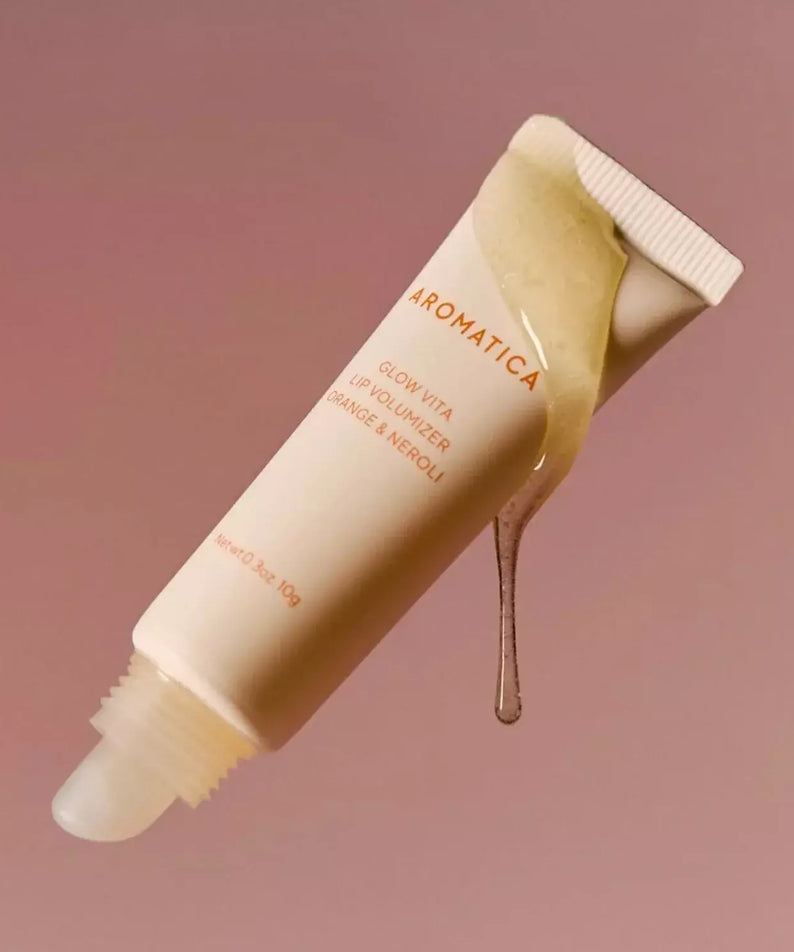 AROMATICA Glow Vita Lip Volumizer Orange & Neroli de la marque AROMATICA, tube sur fond rose, goutte de gloss