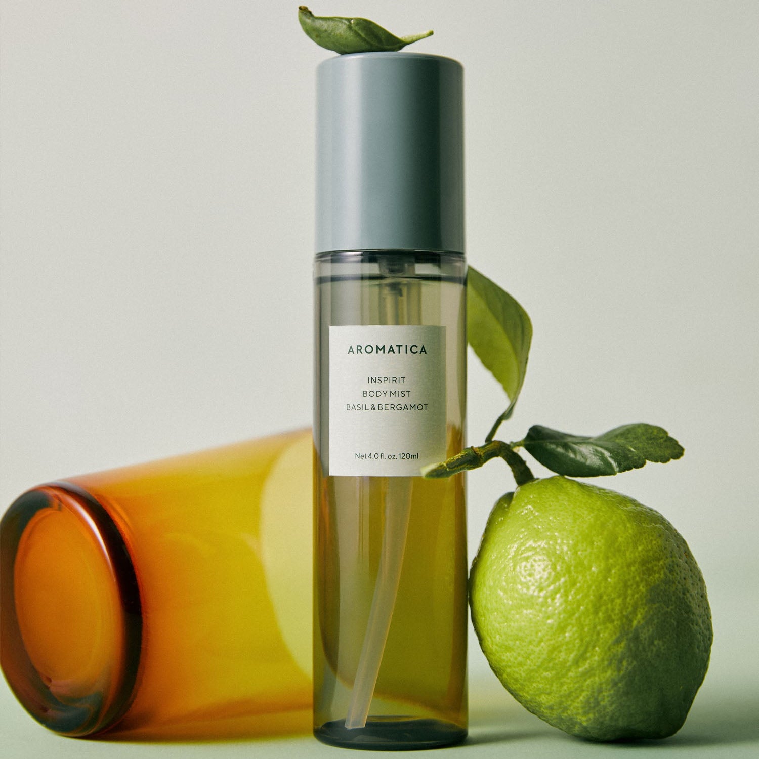 Décris l’image en français : AROMATICA Inspirit Body Mist Basil & Bergamot 120ML, flacon sur fond clair avec basilic et citron.