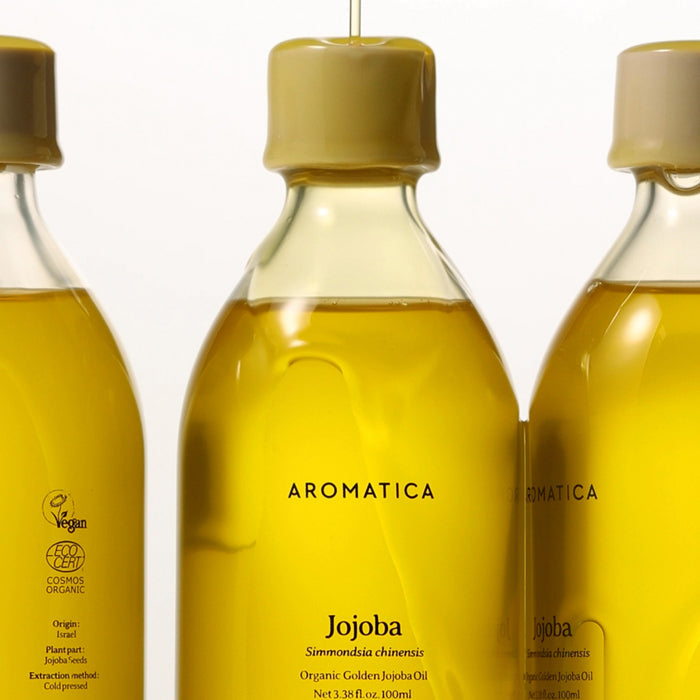 AROMATICA Organic Golden Jojoba Oil 100ml, flacons d'huile dorée en arrière-plan blanc, marque bien visible.