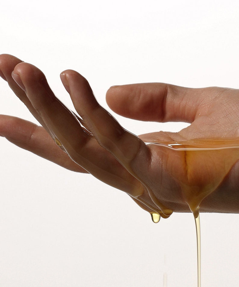 AROMATICA Organic Golden Jojoba Oil 100ml, flacon sur main, huile dorée s’écoulant, contexte beauté soin peau