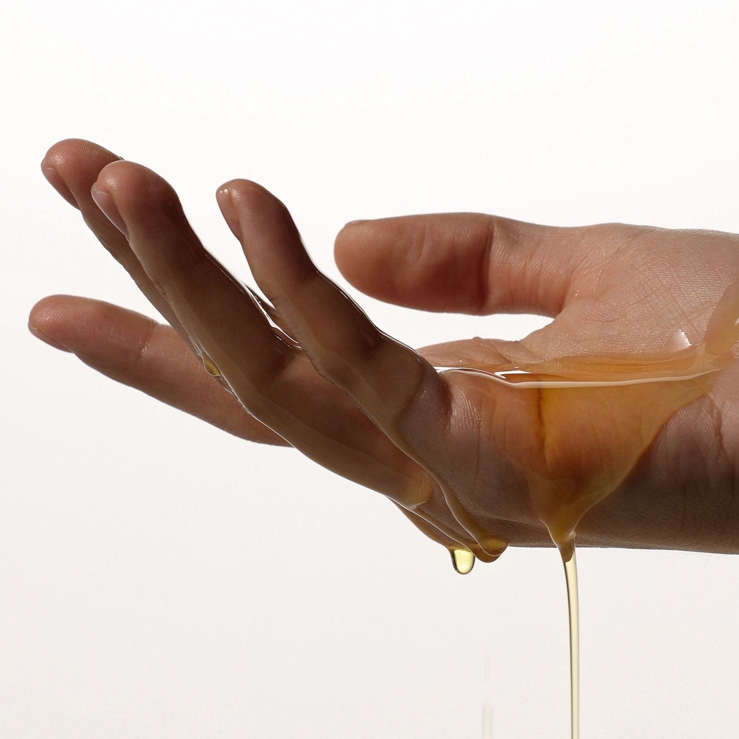 AROMATICA Organic Golden Jojoba Oil 100ml, flacon sur main, huile dorée s’écoulant, contexte beauté soin peau