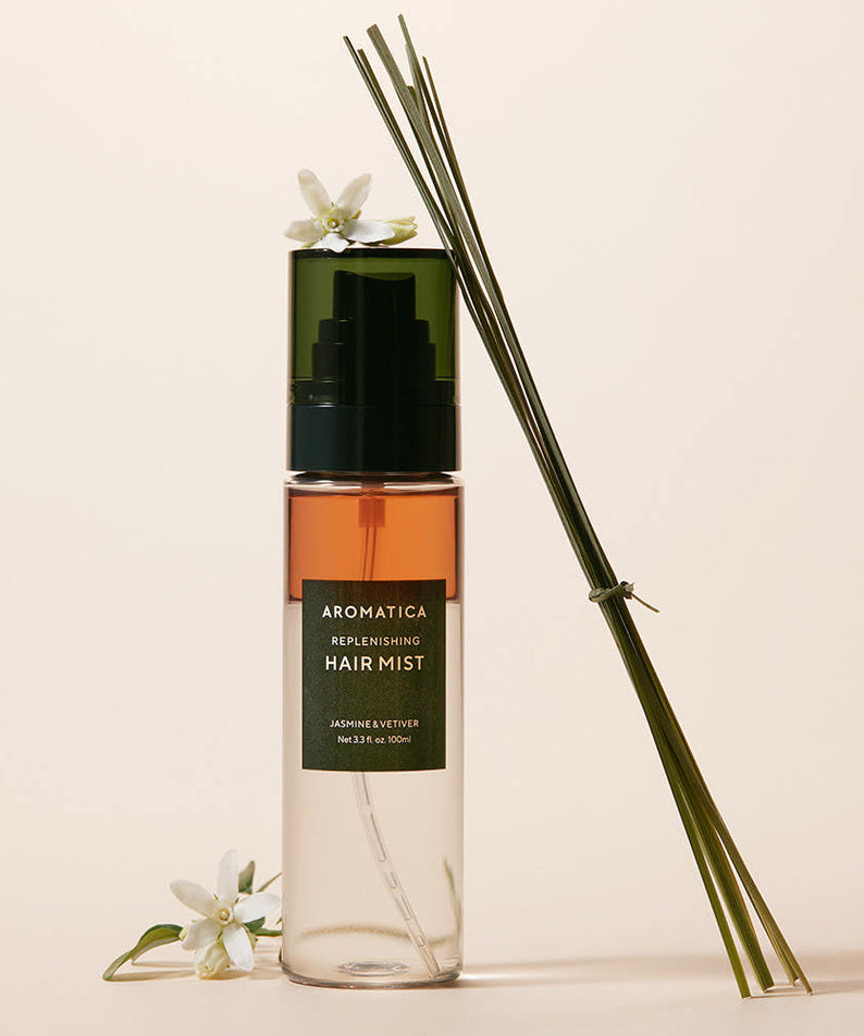 AROMATICA Replenishing Hair Mist Jasmine & Vetiver 100ml, flacon sur fond beige avec fleurs blanches et diffuseur d’ambiance.