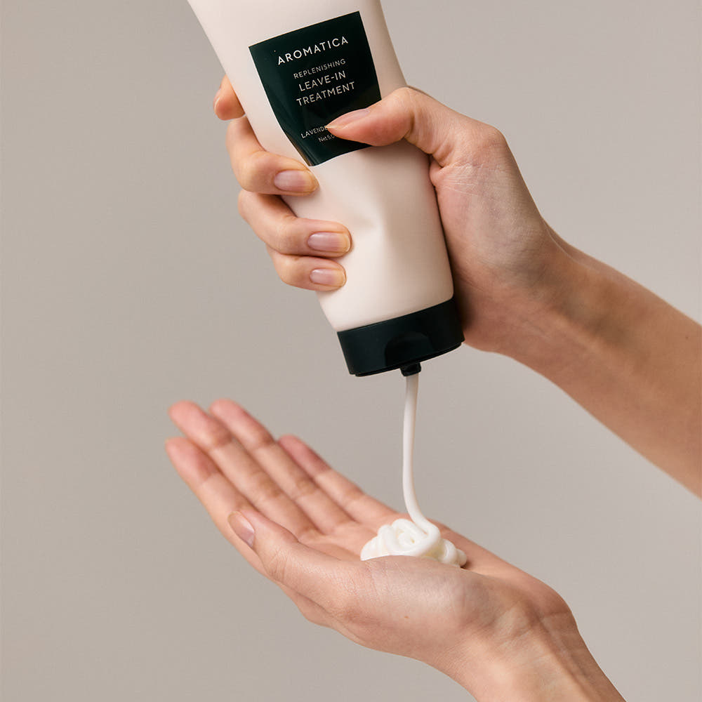 AROMATICA Replenishing Leave-In Treatment Lavender & Patchouli 150ML, crème sur mains, tube entre mains, fond beige