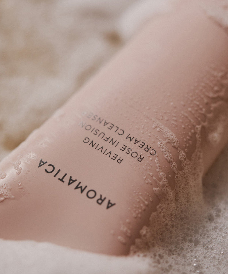 AROMATICA Reviving Rose Infusion Cream Cleanser 145ML, bouteille et mousse sur peau, ambiance spa, gros plan.