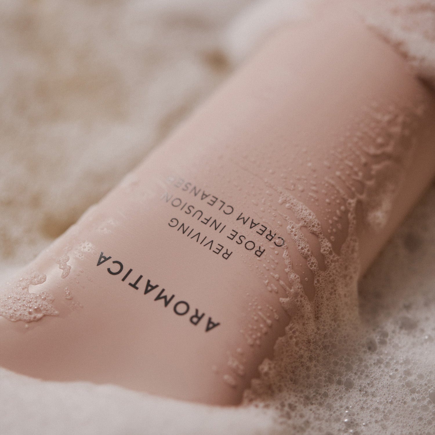AROMATICA Reviving Rose Infusion Cream Cleanser 145ML, bouteille et mousse sur peau, ambiance spa, gros plan.
