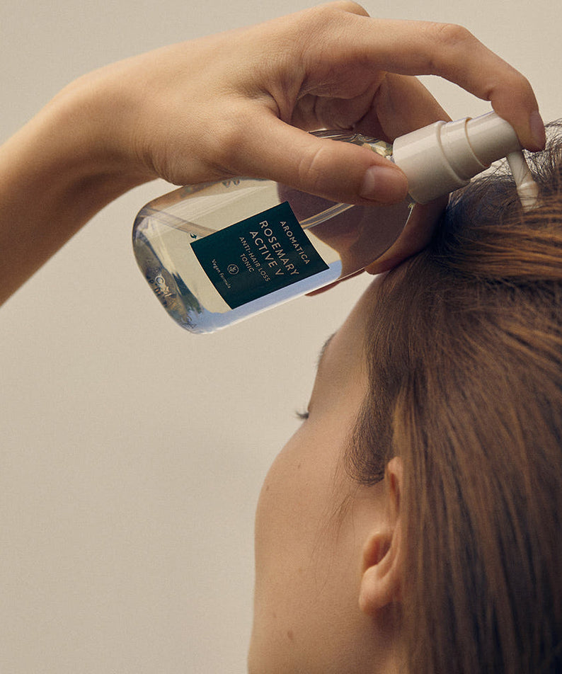 AROMATICA Rosemary Active V Anti-Hair Loss Tonic 100ML : main applique sur cheveux, femme en salle de bain, flacon AROMATICA visible
