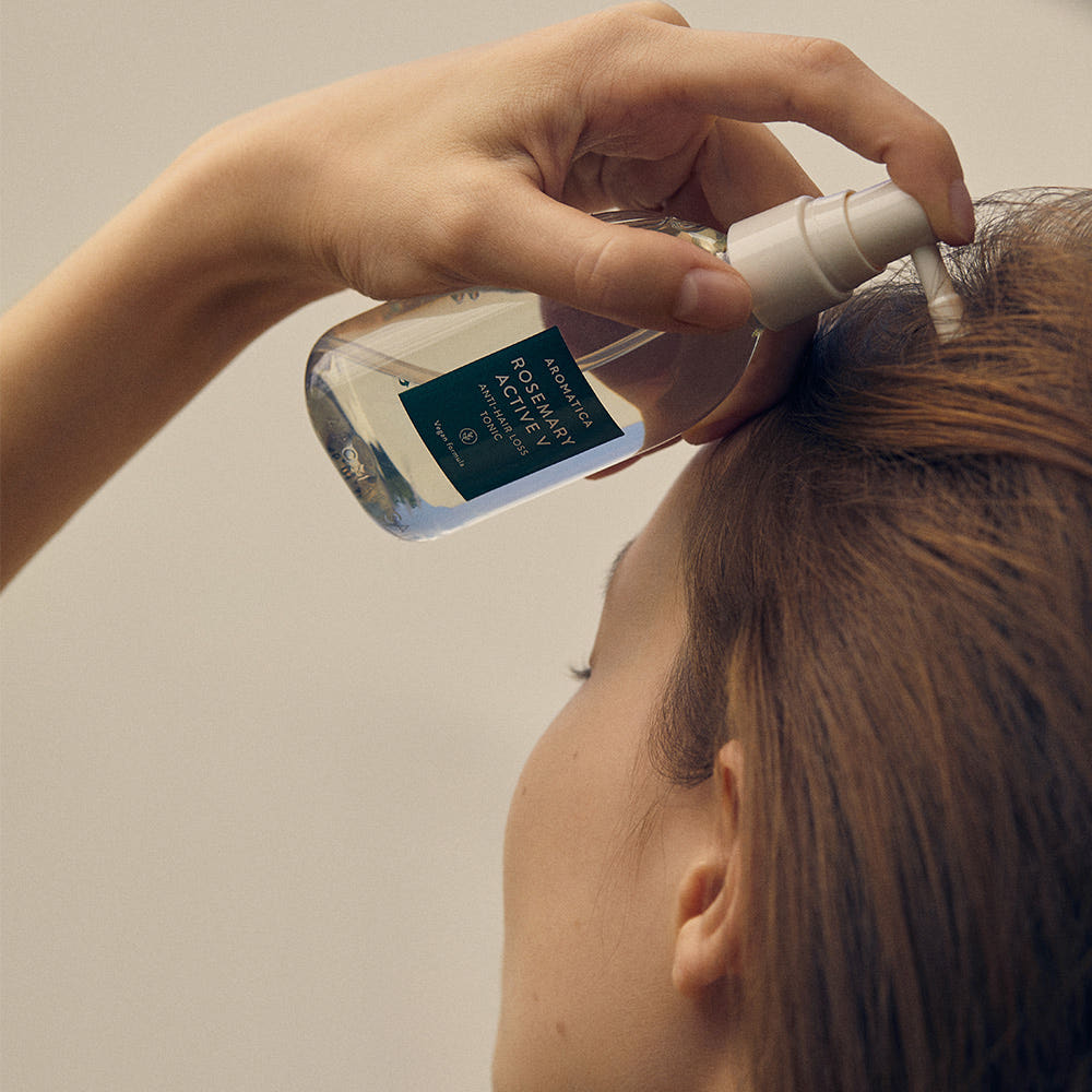 AROMATICA Rosemary Active V Anti-Hair Loss Tonic 100ML : main applique sur cheveux, femme en salle de bain, flacon AROMATICA visible