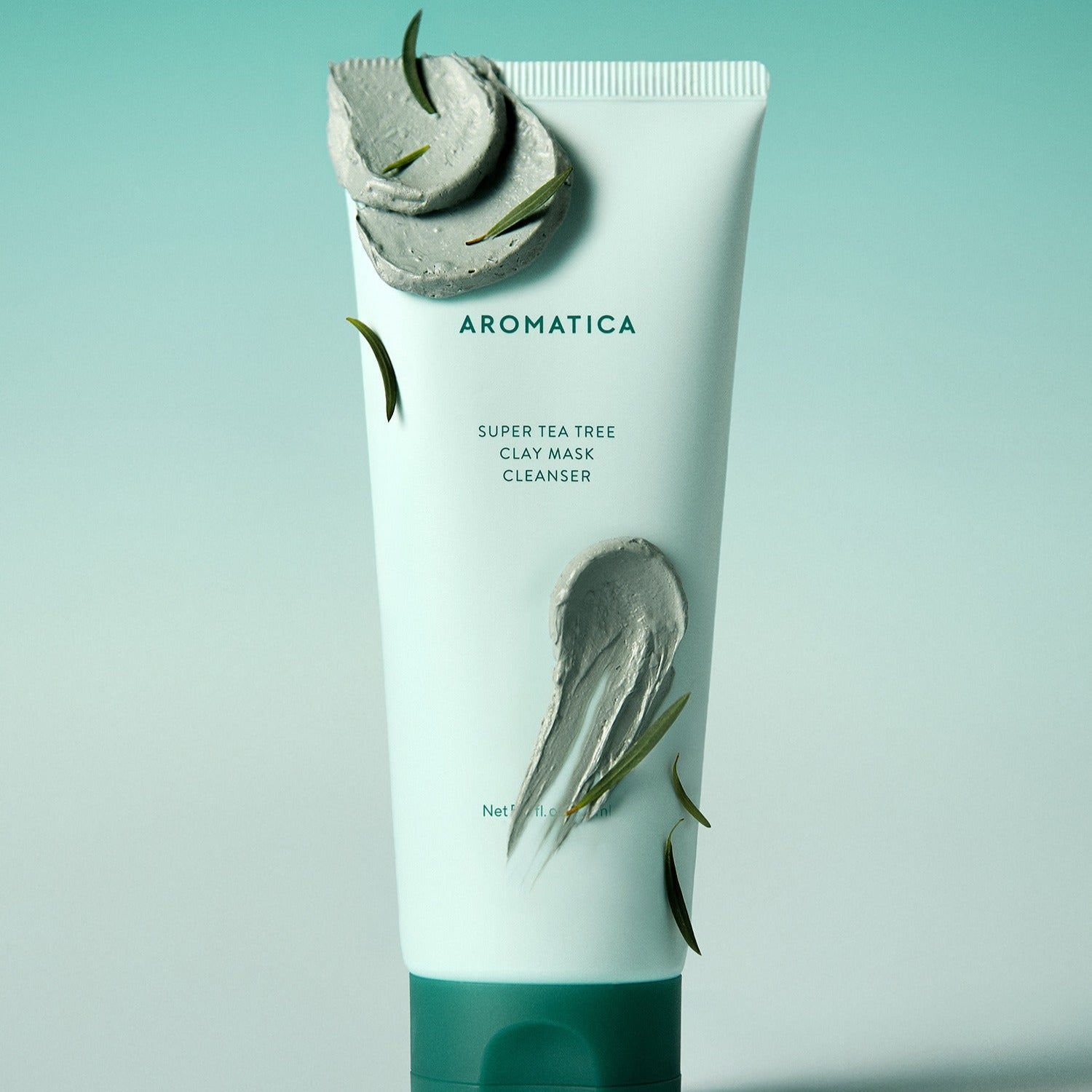 Décrivez l'image en français : AROMATICA Super Tea Tree Clay Mask Cleanser 150ML, tube vert sur fond bleu, feuilles de thé.