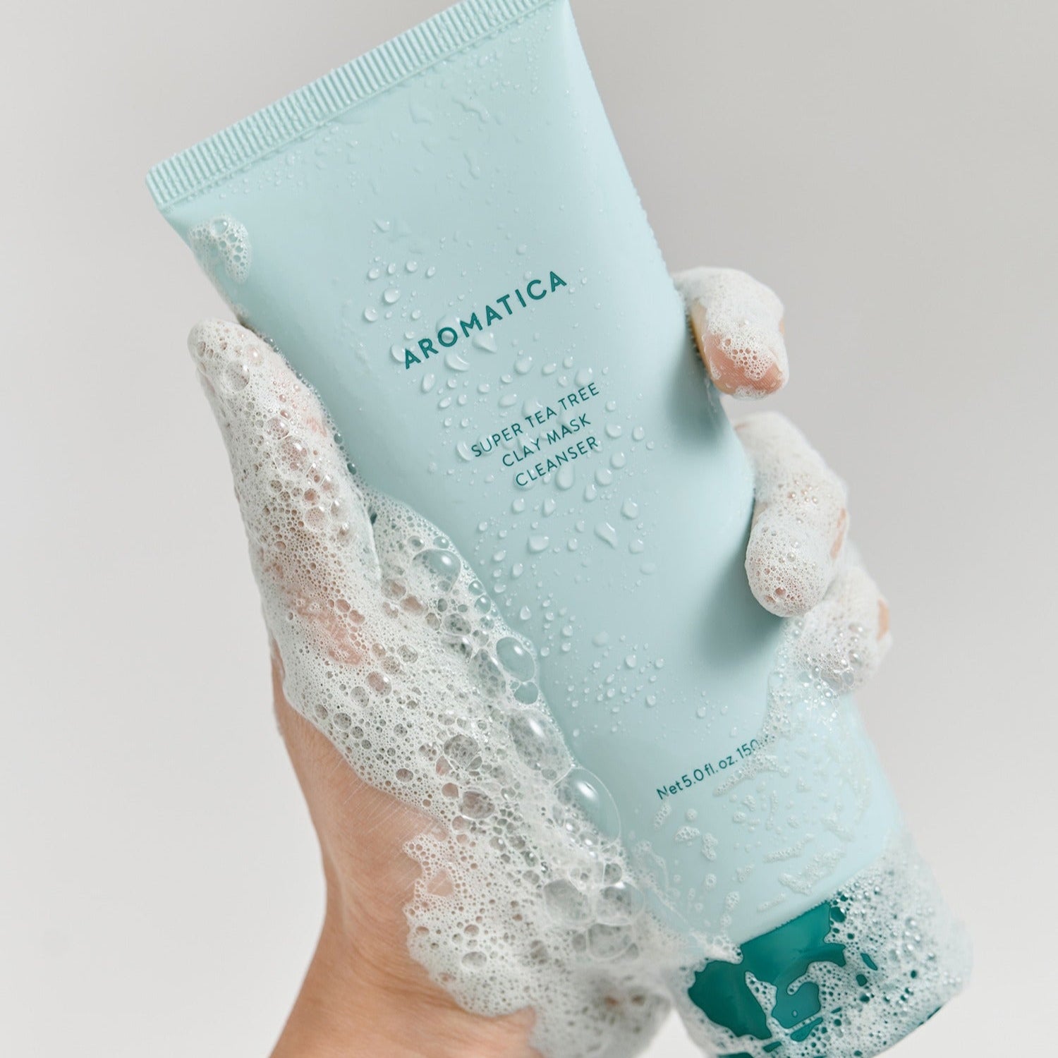 AROMATICA Super Tea Tree Clay Mask Cleanser 150ML de la marque, tube bleu, mains sous mousse sur fond blanc
