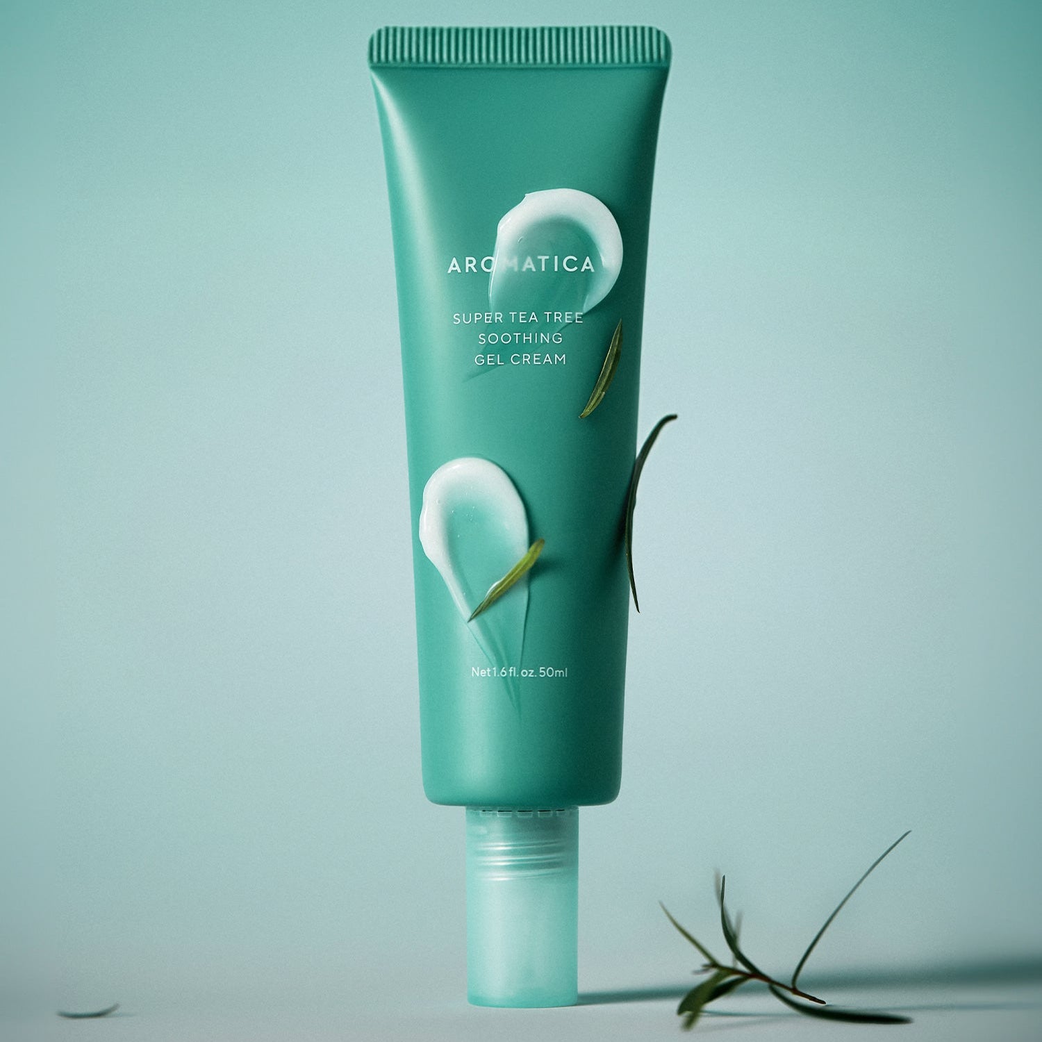 AROMATICA Super Tea Tree Soothing Gel Cream 50ML : tube vert sur fond bleu, brins d’arbre à thé, studio produit.