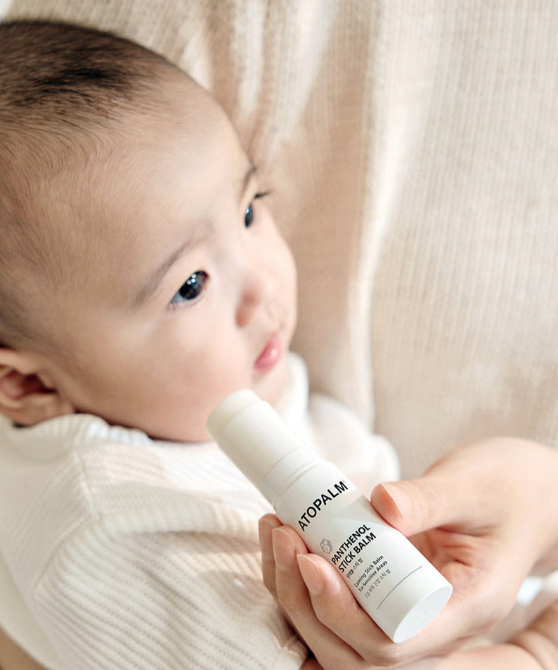 Bébé tenant le baume stick ATOPALM Panthenol Stick Balm 10g pour peau sensible, hydratation et protection douce au quotidien.