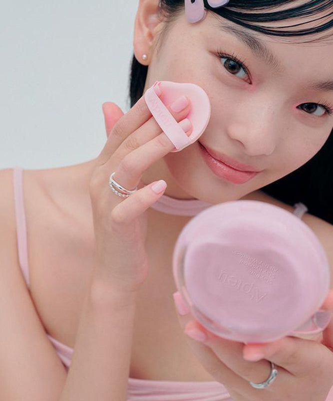 Jeune femme appliquant A'PIEU Waterlock Comfort Veil Cushion 15g avec un applicateur rose, montrant un teint frais et soigné.