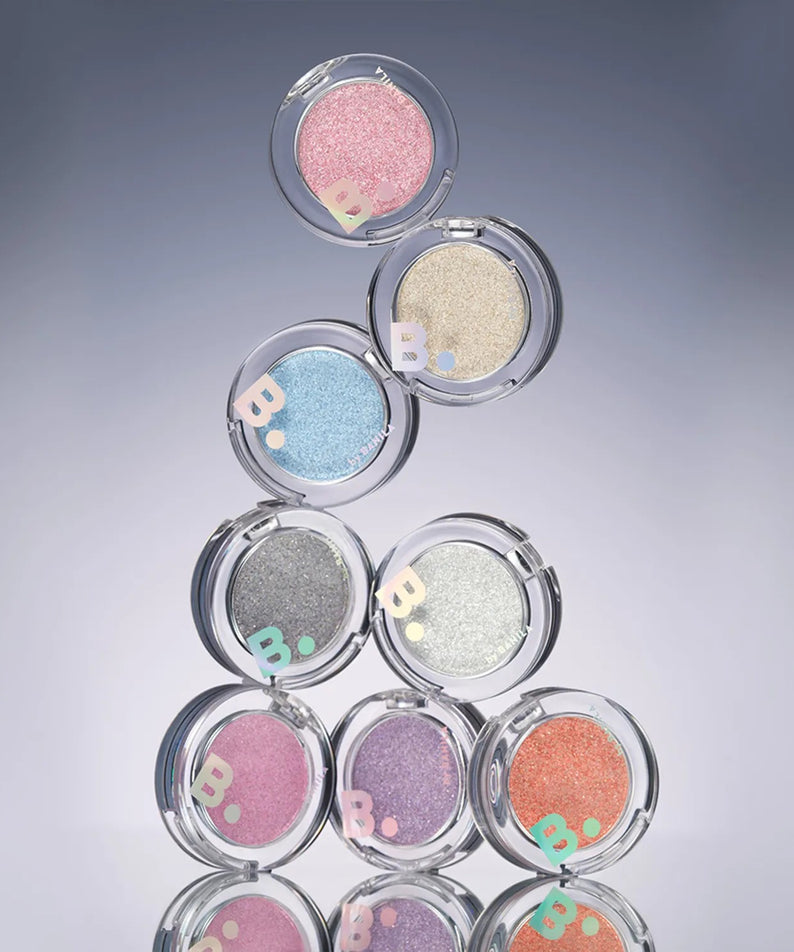 BANILA CO Hyper Holobeam Eye Glitter, maquillage yeux en fards scintillants roses, dorés et bleus sur fond bleu.