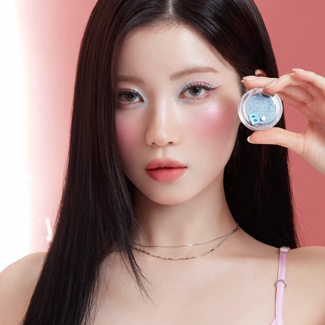 BANILA CO Hyper Holobeam Eye Glitter de la marque BANILACO, maquillage scintillant sur un œil, photo beauté sur fond rose.