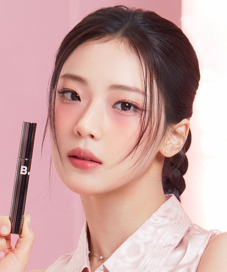 BANILA CO Powerproof Mascara de BANILACO, maquillage yeux sur fond rose, modèle en gros plan tenant le mascara.