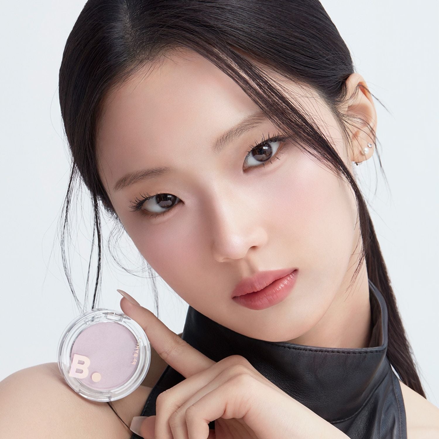 Décris l'image en français : BANILA CO Silky Glow Highlighter, jeune femme maquillée, pot rose sur fond clair, éclat lumineux.