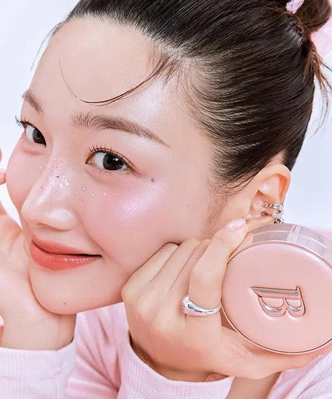 Femme souriante tenant BANILACO Essence Skin Pink Cushion, maquillage lumineux et éclat parfait en rose.