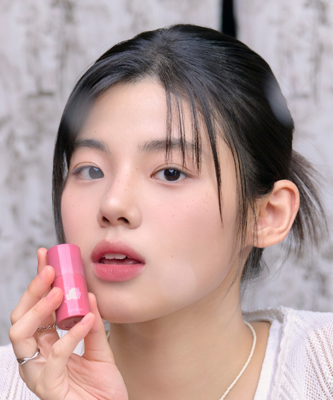 ROMAND Bare Water Tint de la marque ROMAND, sur fond marbre : une femme tient le baume rose près du visage.