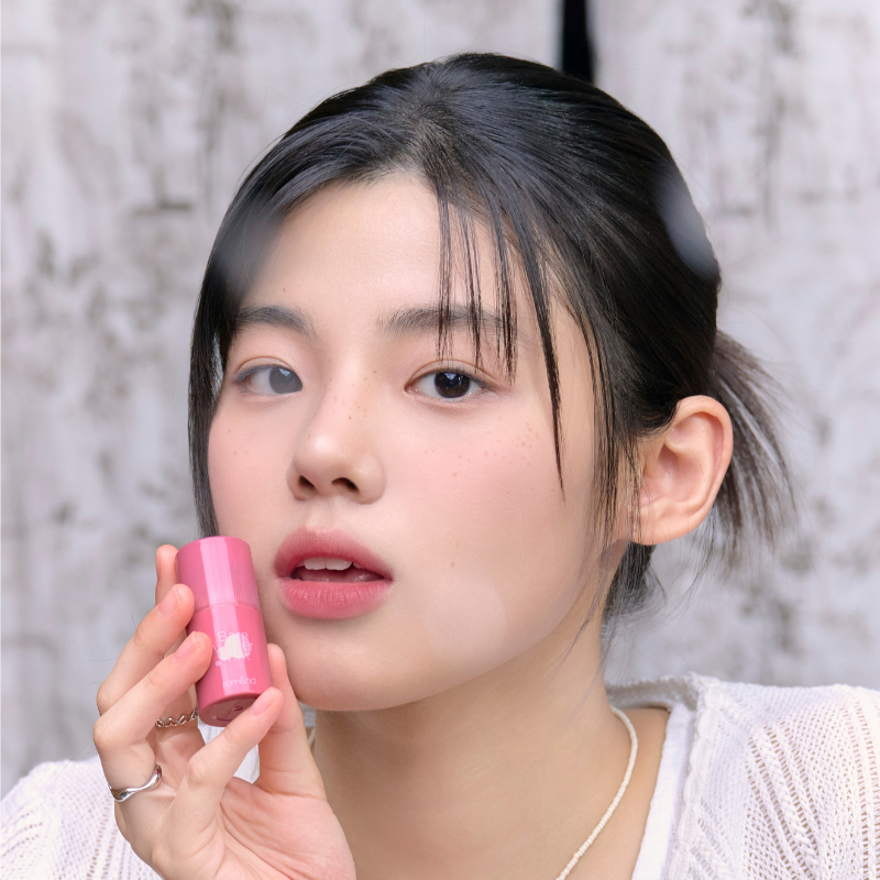 ROMAND Bare Water Tint de la marque ROMAND, sur fond marbre : une femme tient le baume rose près du visage.