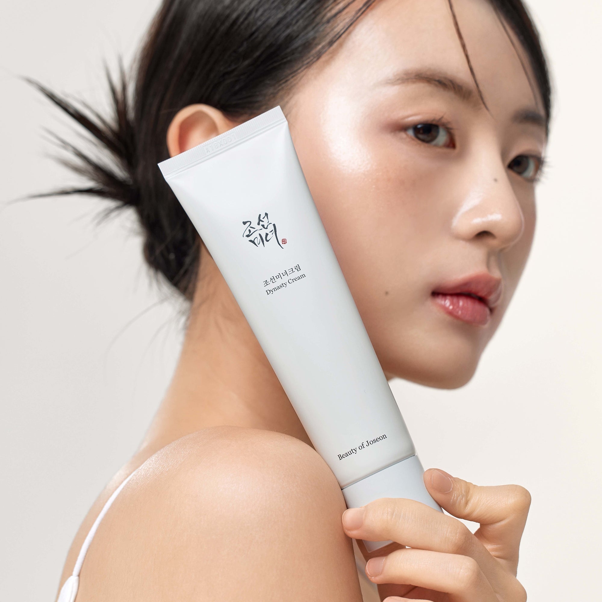 BEAUTY OF JOSEON Dynasty Cream 100ml, tube blanc sur peau, portrait beauté fond clair, marque et produit en évidence