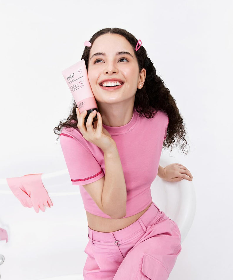 Femme souriante tenant le BELIF Super Knights Pore Fiming Vegan Pack Cleanser 150ml, vêtue de rose dans une salle de bain.