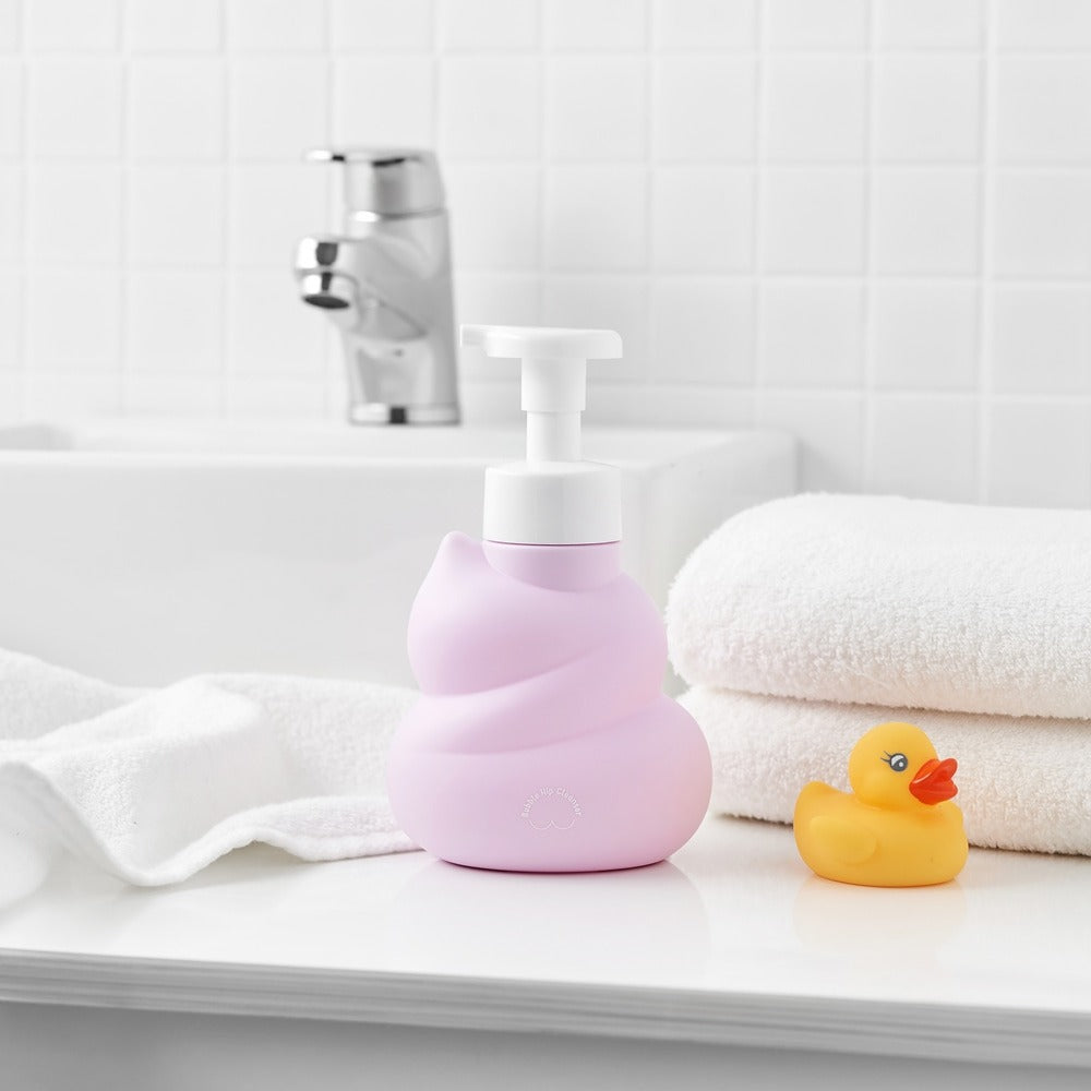Décris l'image en français : BELLBOY STUDIO Hippong Bubble Butt Cleanser en flacon rose sur serviettes, salle de bain.