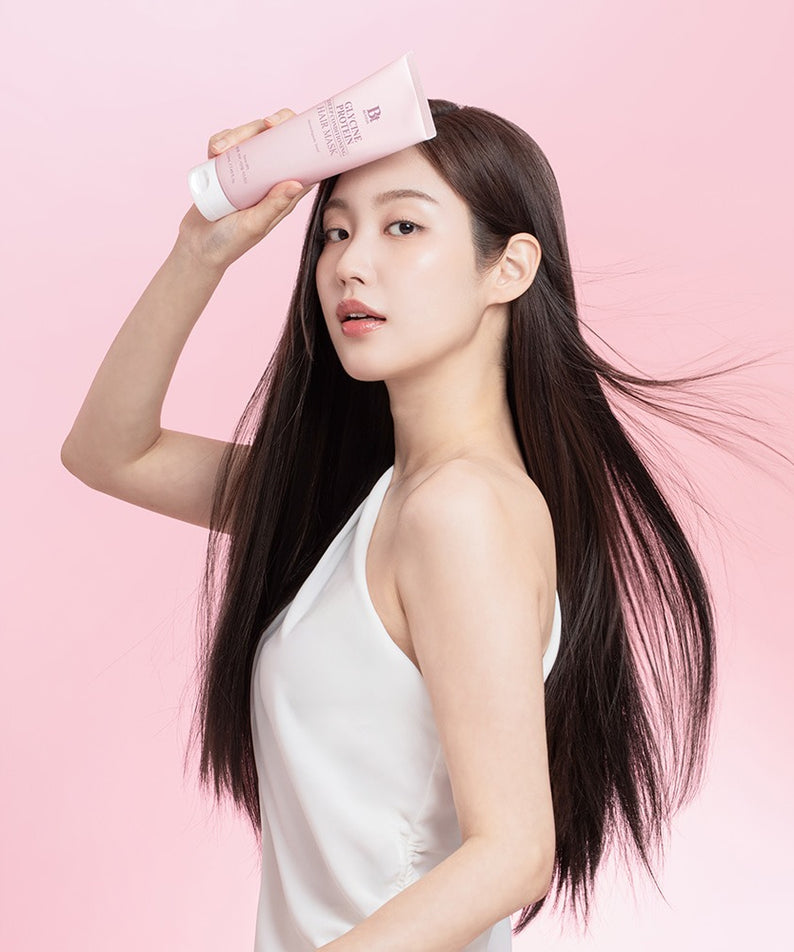 BENTON Glycine Protein Deep Conditioning Hair Mask 220ml, flacon posé sur une femme, cheveux brillants, fond rose.