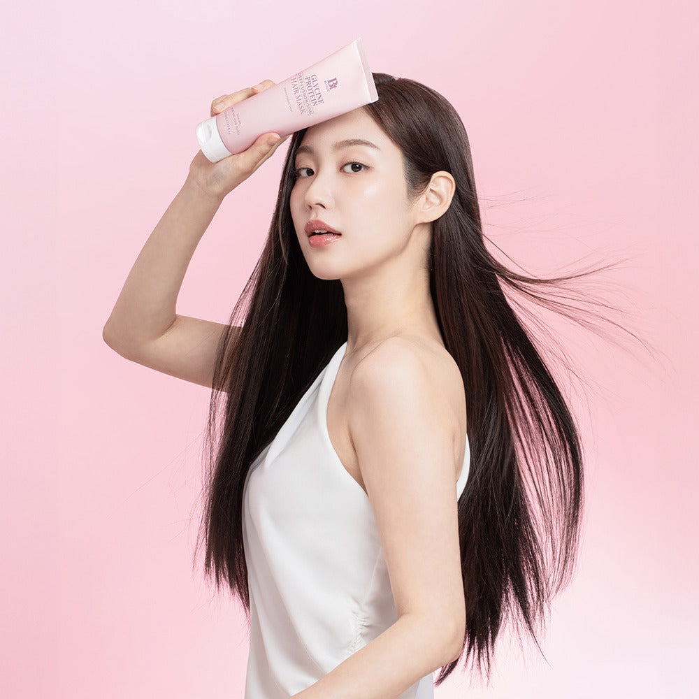 BENTON Glycine Protein Deep Conditioning Hair Mask 220ml, flacon posé sur une femme, cheveux brillants, fond rose.