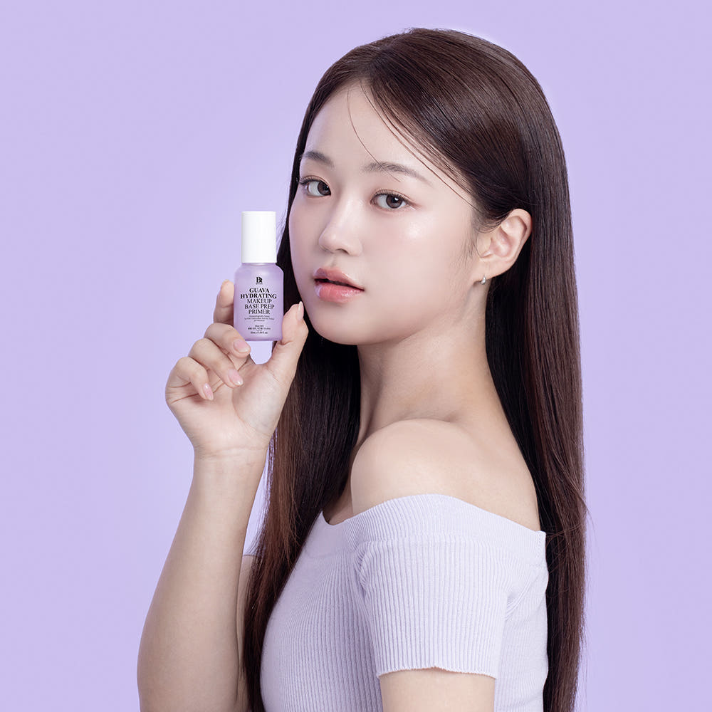 Décris l'image en français : BENTON Guava Moisture Makeup Base Prep Primer 35ml, femme tient le flacon sur fond violet.