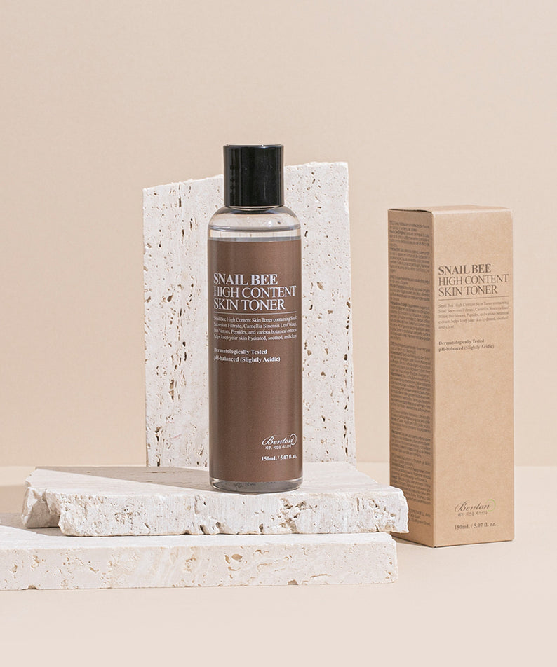Décris l'image en français : BENTON Snail Bee High Content Skin Toner 150ml, bouteille sur socle et boîte, fond beige clair.