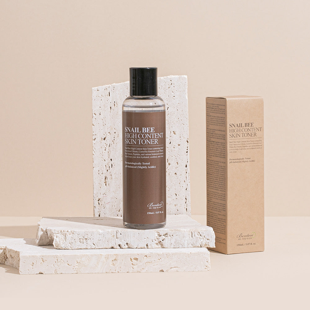 Décris l'image en français : BENTON Snail Bee High Content Skin Toner 150ml, bouteille sur socle et boîte, fond beige clair.