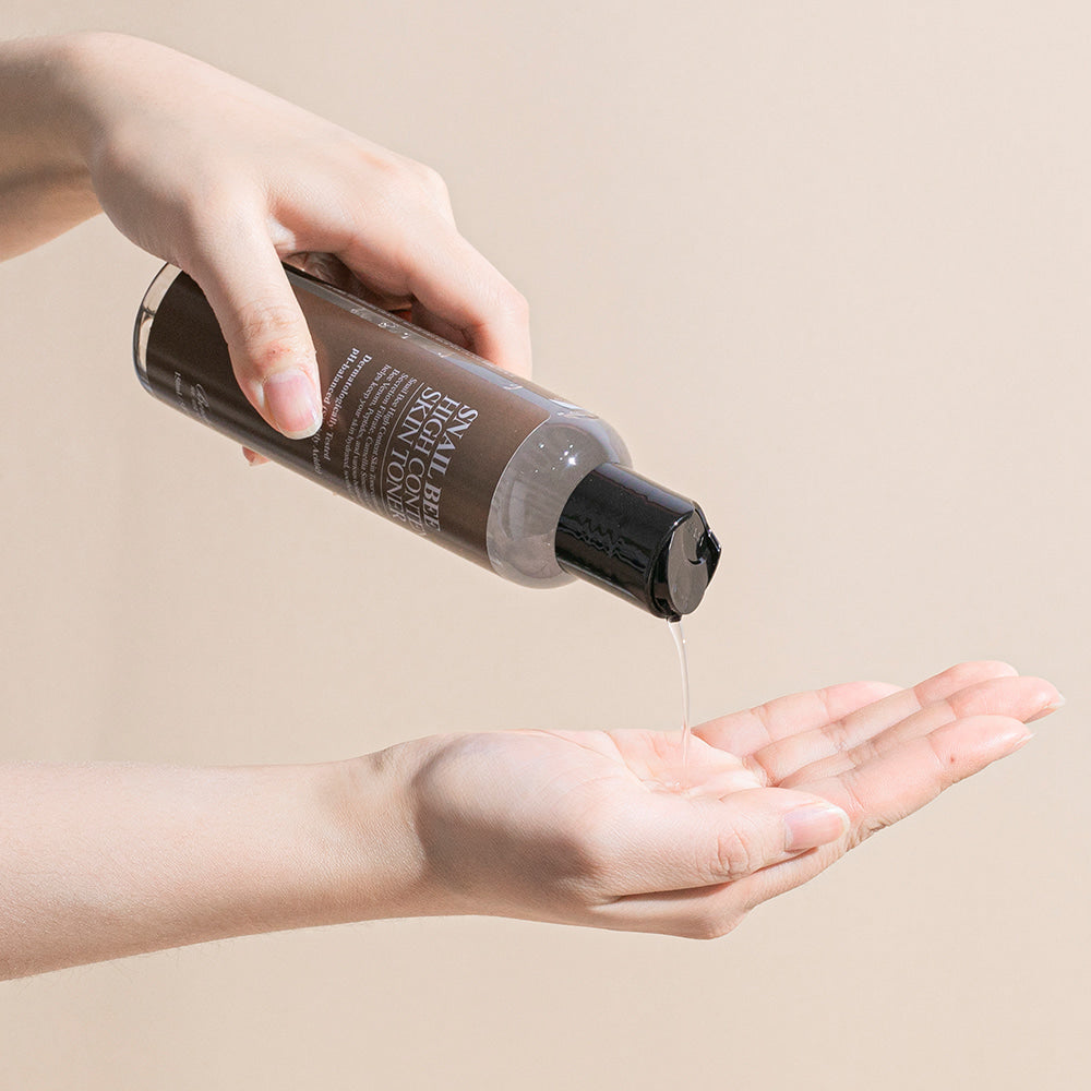 Décrivez l'image en français : BENTON Snail Bee High Content Skin Toner 150ml, produit cosmétique sur main, texture versée.