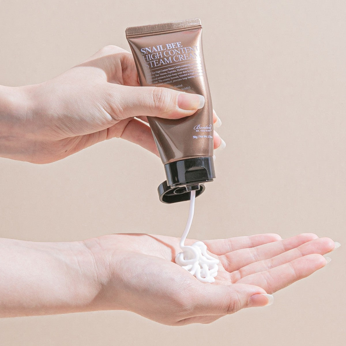Main tenant le BENTON Snail Bee High Content Steam Cream 50g, marque BENTON, crème sur la main, fond clair