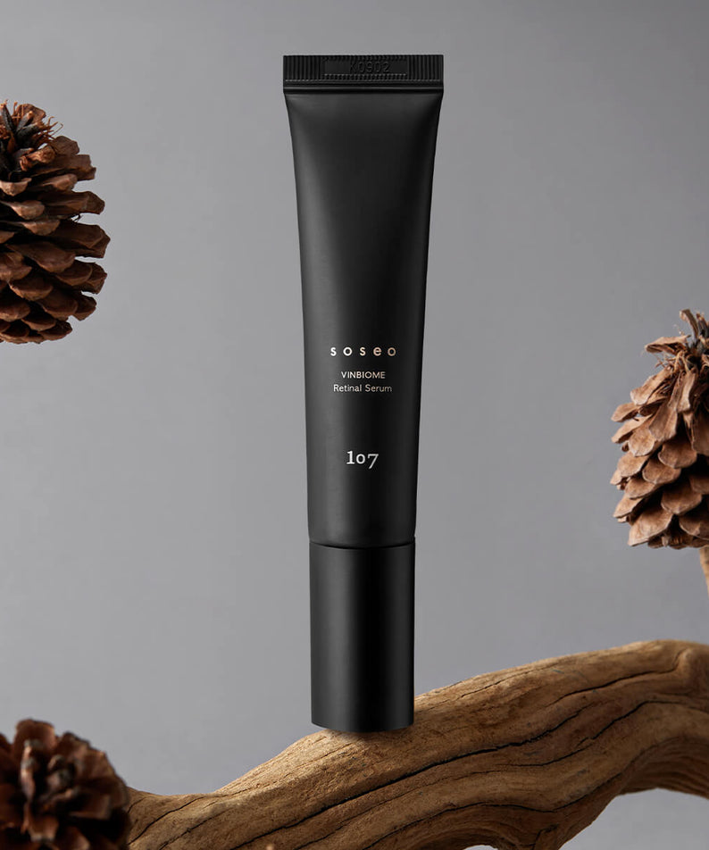107 Soseo Vinbiome Retinal Serum 20ml : tube noir sur fond gris, décor pommes de pin et bois, lumière studio.