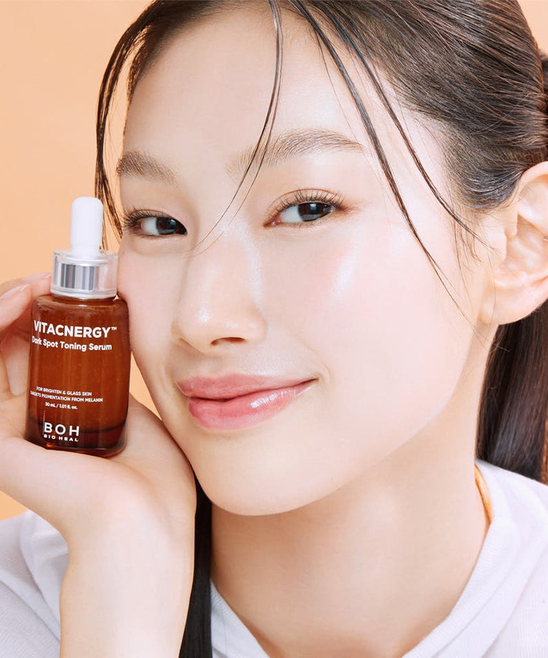 BIO HEAL BOH Vitacnergy Dark Spot Toning Serum : sérum présenté sur le visage d’une femme, flacon à la main, fond beige.