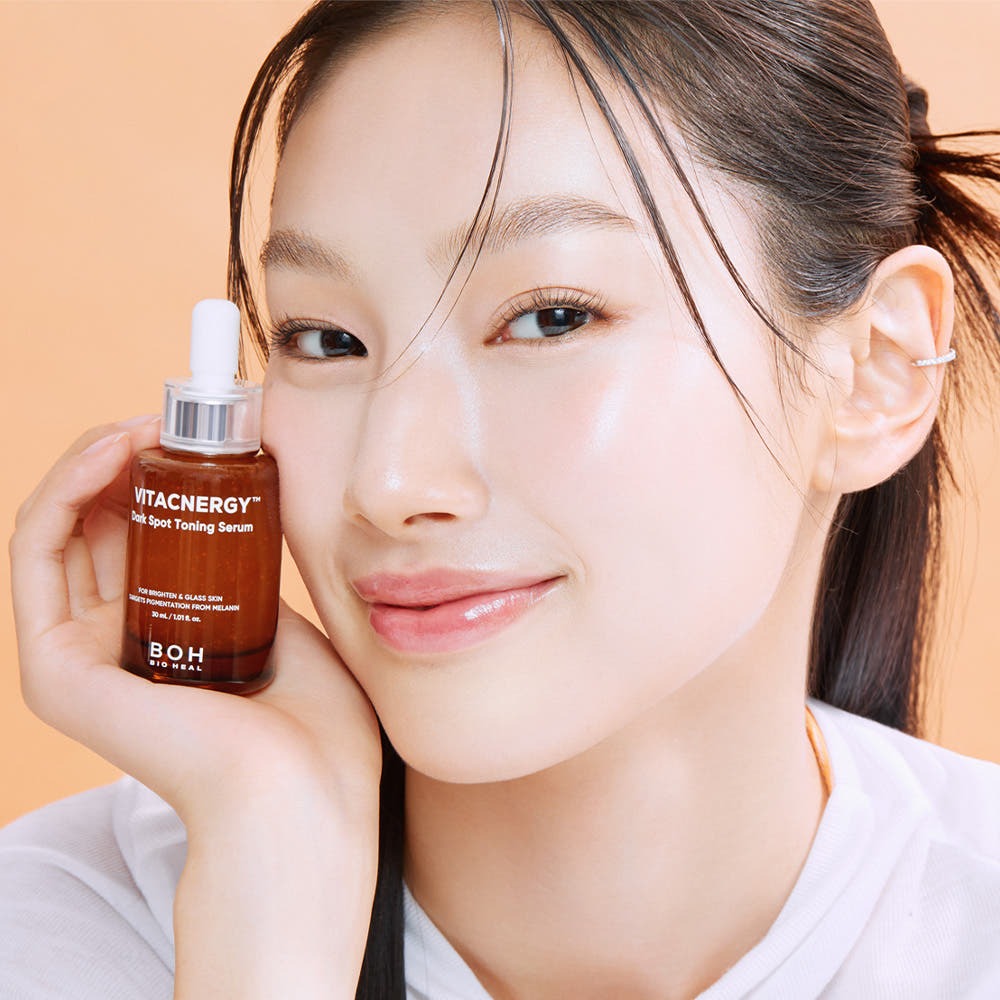 BIO HEAL BOH Vitacnergy Dark Spot Toning Serum : sérum présenté sur le visage d’une femme, flacon à la main, fond beige.