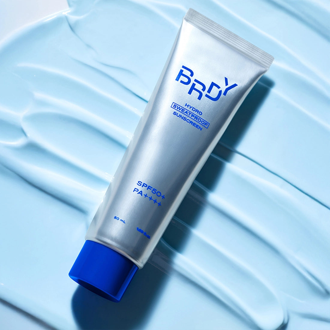 B.READY NEW Hydro Sweatproof Sunscreen 50ml, tube sur tissu bleu texturé, contexte sportif anti-transpiration.